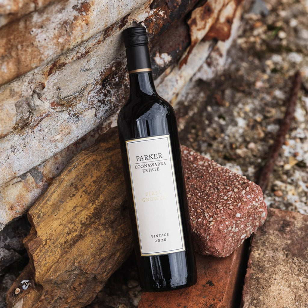 A bottle of Parker Coonawarra Estate First Growth Cabernet Sauvignon 2020 red wine, leaning against an old stone wall with red bricks in the foreground.