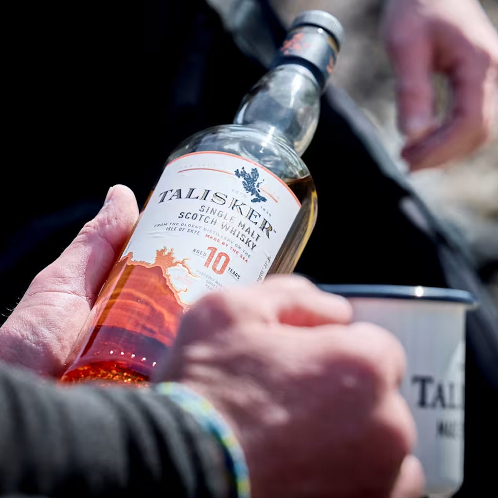 A close up picture of Talisker 10 Year Old Malt Whisky held in a hand with a metal mug in the other hand