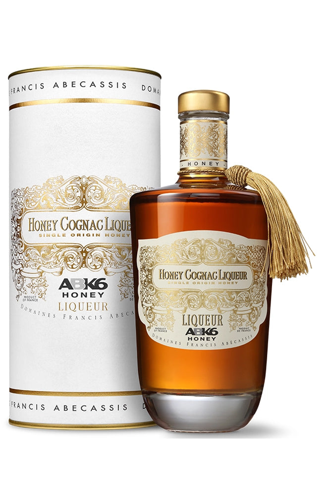 A bottle of ABK6 Honey Cognac Liqueur with a gold tassel next to its white and gold cylindrical packaging box, on a clean white background.