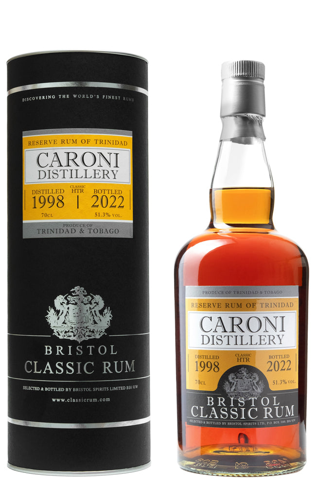 A bottle of Caroni Distillery Bristol Classic Rum next to its black cylindrical packaging box, featuring amber liquid and gold label accents on a white background.